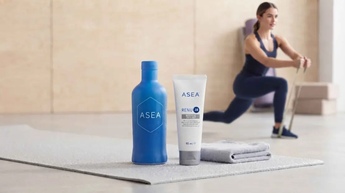 Bottiglia di acqua ASEA redox signaling water e tubetto di gel RENU 28 su tappetino da fitness con atleta sullo sfondo in palestra